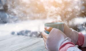 Frau wärmt ihre kalten Hände an einer Tasse heißem Tee
